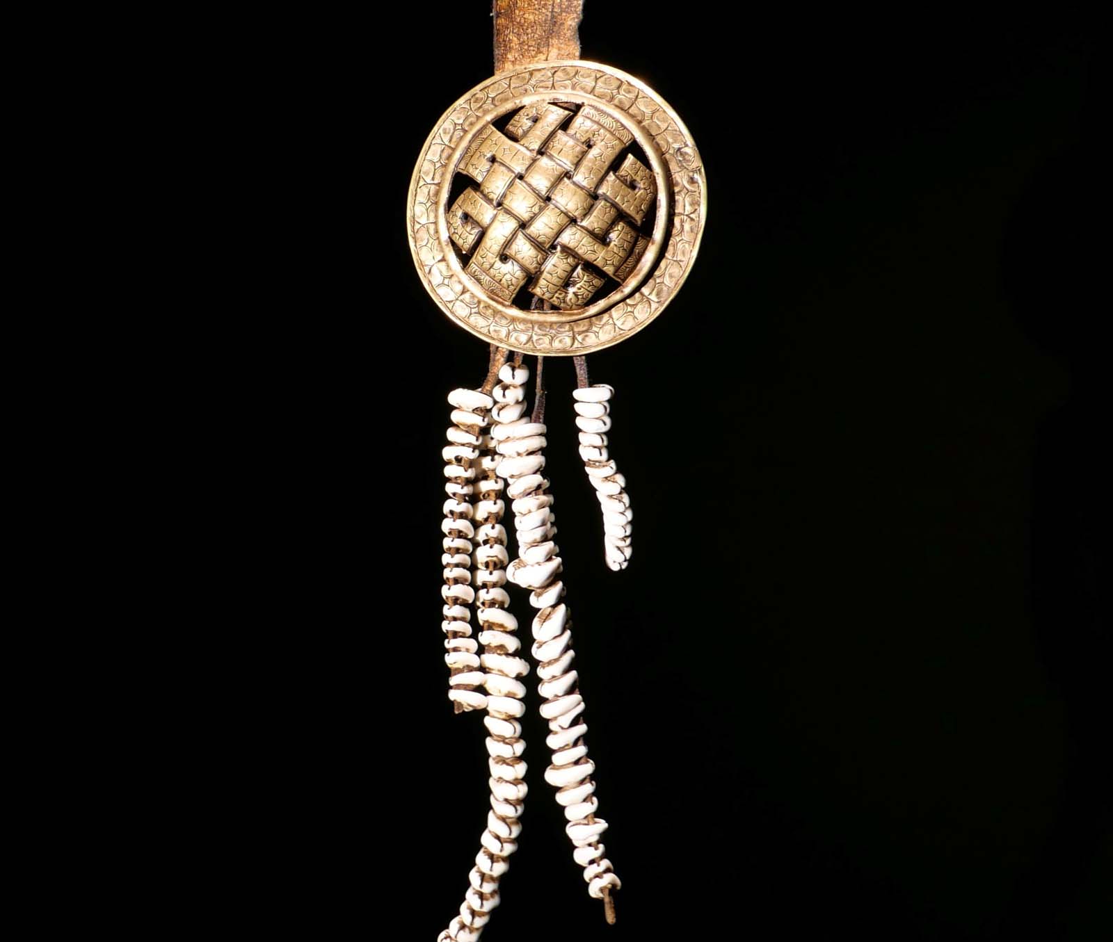 Gürtelschmuck „Ewiger Knoten“ Bronzescheibe an Lederband, Kauri-Anhänger. Mitte 20. Jhdt. Ladakh / Zanskar. H 47 cm. 400.- €