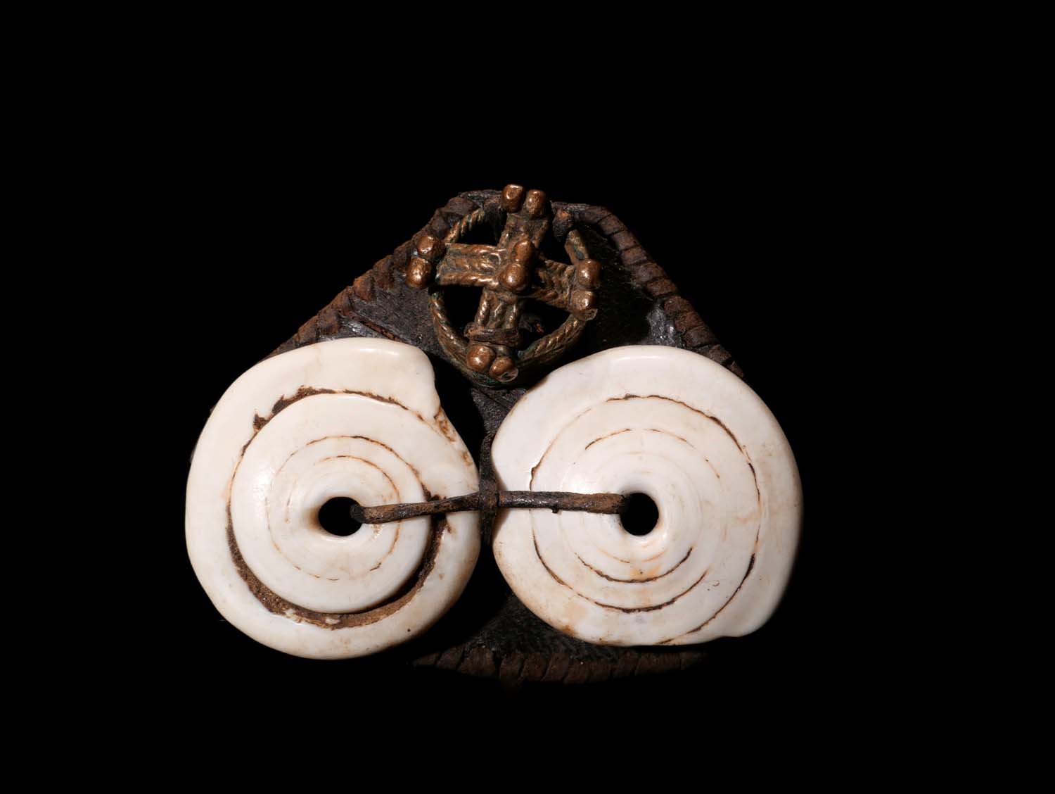 Amulett-Anhänger. Auf Leder aufgenähtes Bronze-Schmuckelement und zwei Scheiben aus Schneckengehäuse. Dogon / Mali.  Mitte 20.Jhdt. B 6 cm. 100.- €